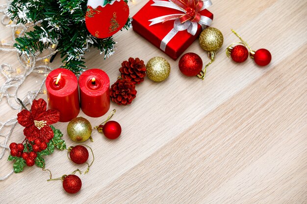 Photo set of christmas decorative items red and gold shiny glossy sphere balls candles present gift box with silver ribbon bowtie light bulb rope pine seeds xmas mockup tree with hanging sock on wood table.