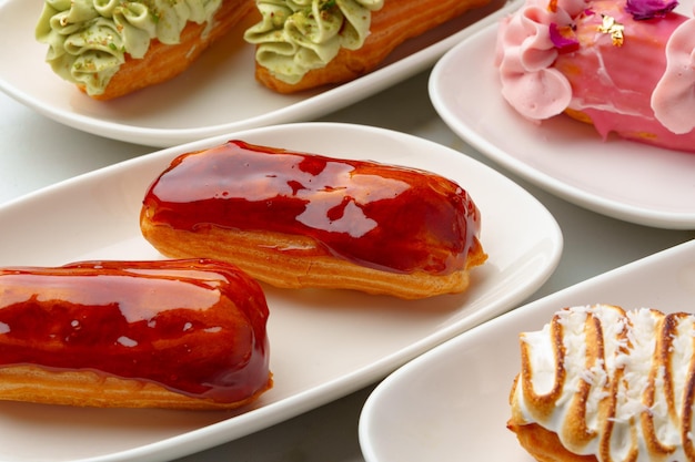 Set of colored eclairs with whipped cream on white plates