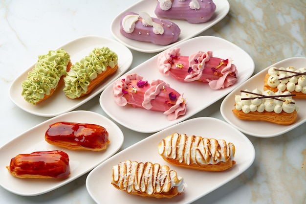 Set of colored eclairs with whipped cream on white plates