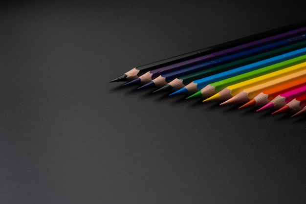 Set of colored pencils, row of wooden colored pencils on black background, for drawing