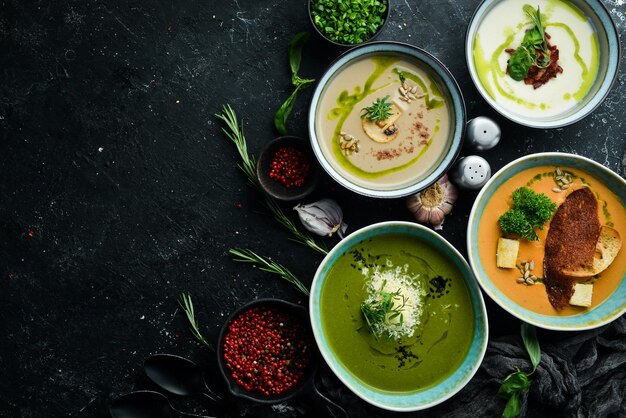 Set of colored soups in bowls on a black stone background Healthy food Top view Rustic style