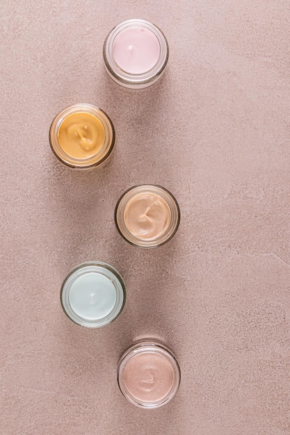 Set of cosmetic cream of various colors in glass jars on beige stone background Top Vertical view of the space Layout for product advertising