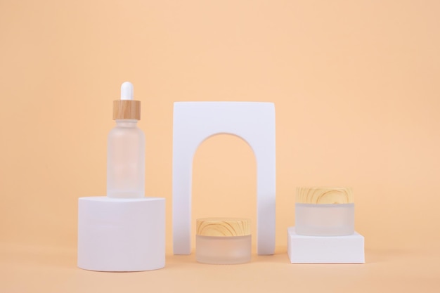 Set of cosmetic products bottles on white podium with arch on beige background