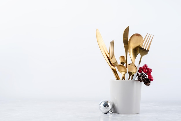 Set of cutlery of spoons knives and forks in cup with holiday decorations on dining table copy space