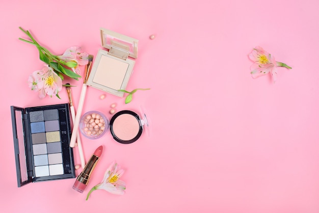 Set of decorative cosmetics with makeup brushes on pink background