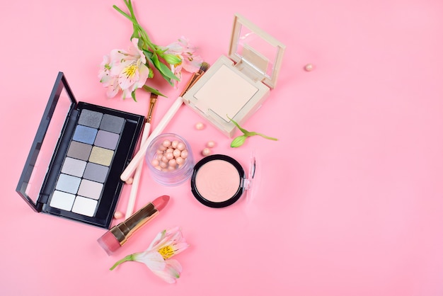 Set of decorative cosmetics with makeup brushes on pink background