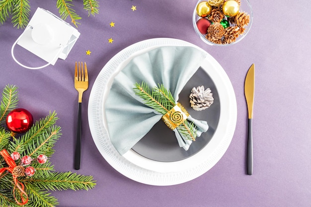 A set of different plates with Christmas decorations and gold cutlery on a gray background surrounded by Christmas decorations top view