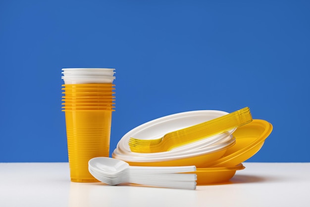 A set of disposable plastic utensils. Yellow and white plates, glasses, forks and spoons. The concep