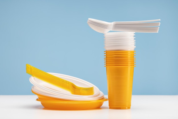 A set of disposable plastic utensils. Yellow and white plates, glasses, forks and spoons.