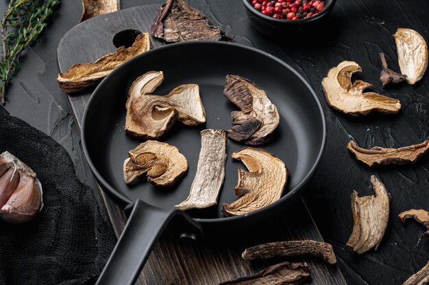 Set of dried mushrooms set in cast iron frying pan, on black background