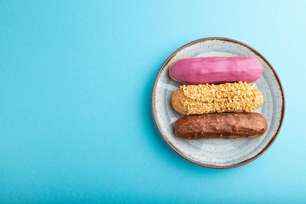 Set of eclair traditional french dessert on ceramic plate on blue pastel background top view copy space