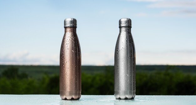 Photo set of eco reusable thermo bottles with plug, sprayed with water. bronze and silver of color. close-up