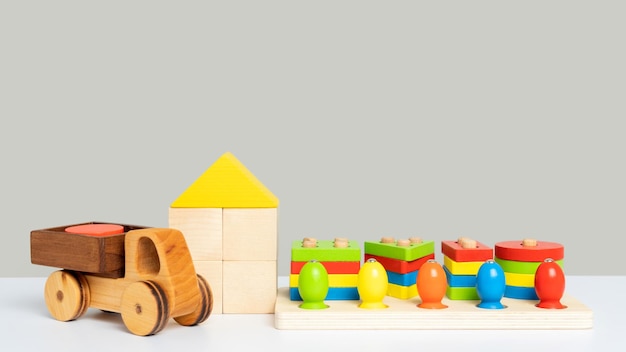 A set of ecofriendly children's educational toys made of wood on a gray background A sorter with various geometric shapes a wooden truck and a constructor made of cubes