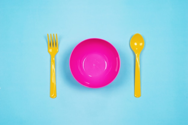 Set of empty pink plastic tableware bowls, yellow spoons and forks