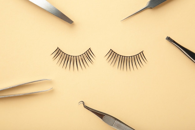 Set of false eyelashes extencions on beige background with tweezers. Minimalism. Top view