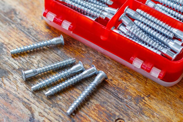 Set of fasteners for assembling furniture in red plastic storage box on wooden table