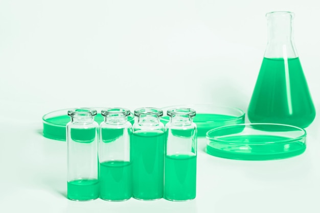 A set of flasks jars for the laboratory with a green liquid Against the background of laboratory glassware Petri dishes flasks test tubes On a white light background