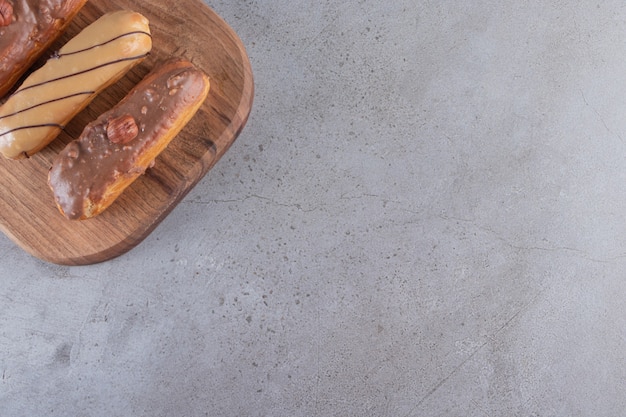 Set of four eclairs with various fillings on wooden cutting board. 