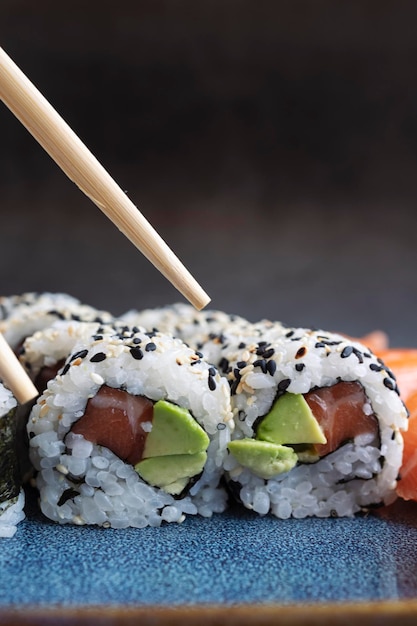 A set of fresh sushi rolls with salmon avocado and sesame seeds with chopsticks