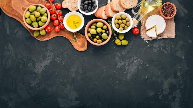 A set of green olives and black olives bread cheese and spices On a black stone table Free space for text