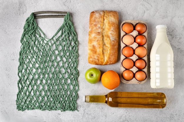 Set of grocery items with healthy food in eco string bag milk oil bread flat lay on gray background