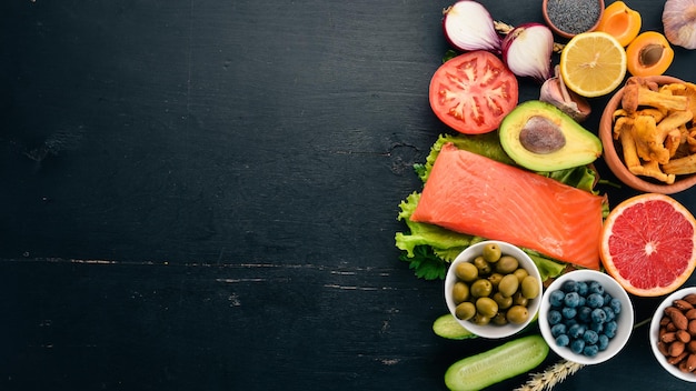 A set of healthy food Fish nuts protein berries vegetables and fruits On a black wooden background Top view Free space for text