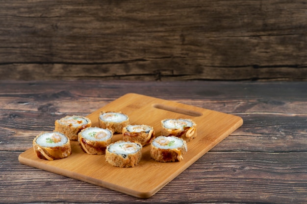 Set of hot fried sushi rolls with salmon on wooden board. 