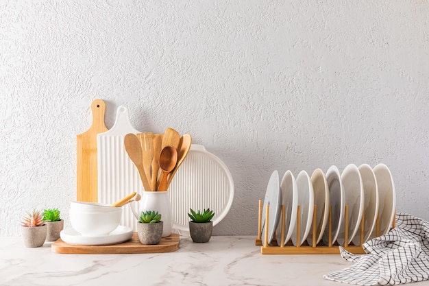 A set of kitchen utensils and dishes in light colors on a marble white countertop against the background of a gray textured wall interior background