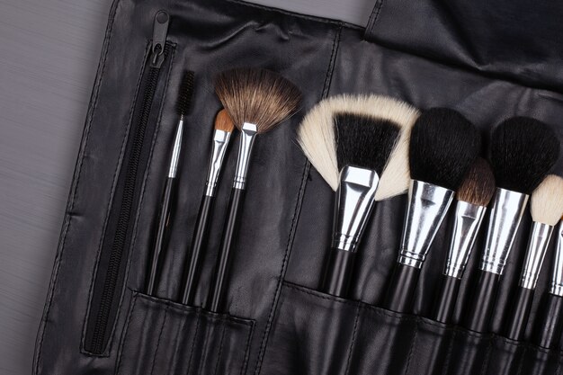 Set of makeup brushes in a leather case, face shadow brushes on gray background.