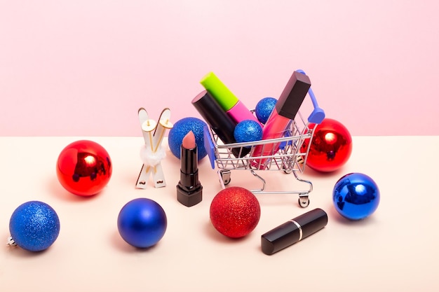 A set of makeup cosmetics in a shopping cart and Christmas tree decorations Lipstick and mascara with Christmas accessories Buying Christmas gifts Winter skin care concept