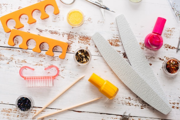 Set of manicure tools and nail polishes on a white wooden background.