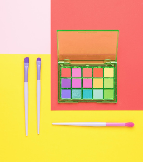 A set of multicolored eye shadow and three brushes on a multicolored background Flat lay