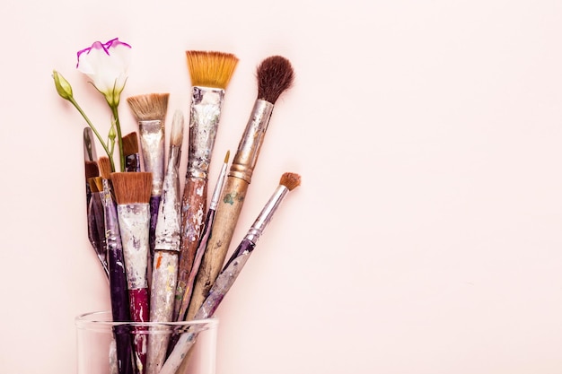 Set of old brushes, flower and palette knife on pale pink background.