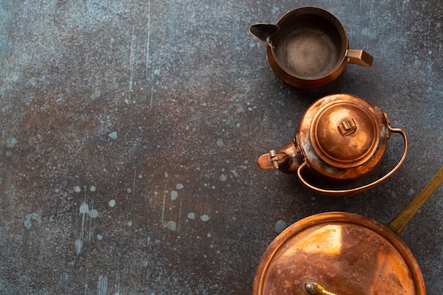 Set of old vintage copper empty tableware on rustic concrete background. Antique copper utensils: pan, teapot, sauce boat. Top view of beautiful aged retro brass cookware from flea market, copy space