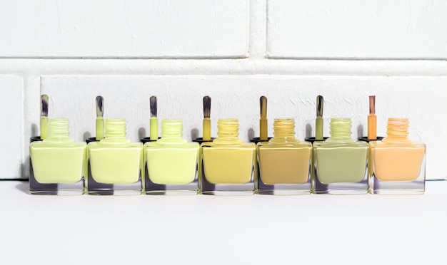 Set of open green tint nail polish bottles with brushes. Group of nail polish on white wall background. Copy space.