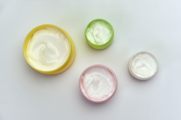 Set of opened multi-colored jars with white cosmetic cream for face and body on a white surface