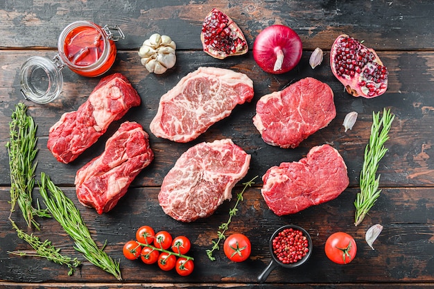 Set  of organic raw beef steakes rump, chuck roll and top blade  cut  with seasonings and herbs on old rustic dark wooden background, top view.