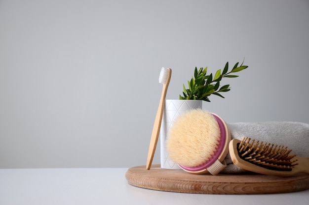 Set of personal eco accessories: tooth brush, body brush, hairbrush and white towel on wooden round board