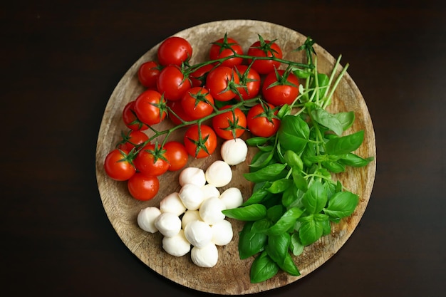 A set of products for caprese salad Tomatoes basil and mozzarella on a wooden board