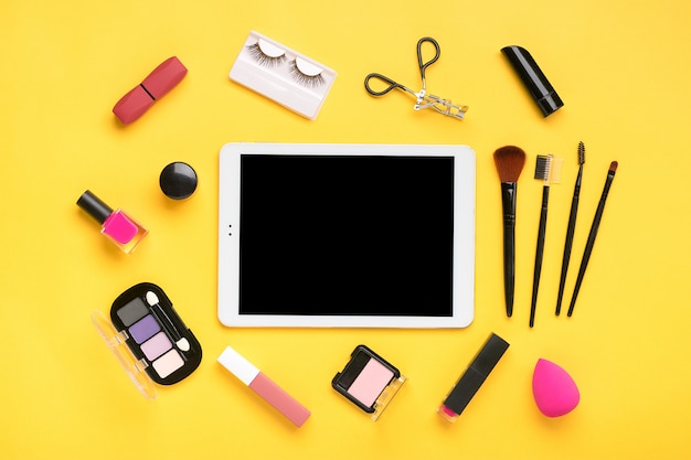 Set of professional cosmetics with a tablet on yellow background