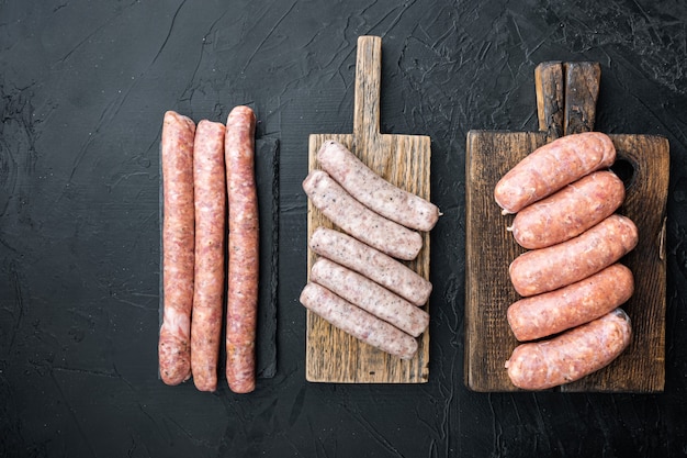 Set of raw pork, beef and chicken sausages, flat lay, on black table