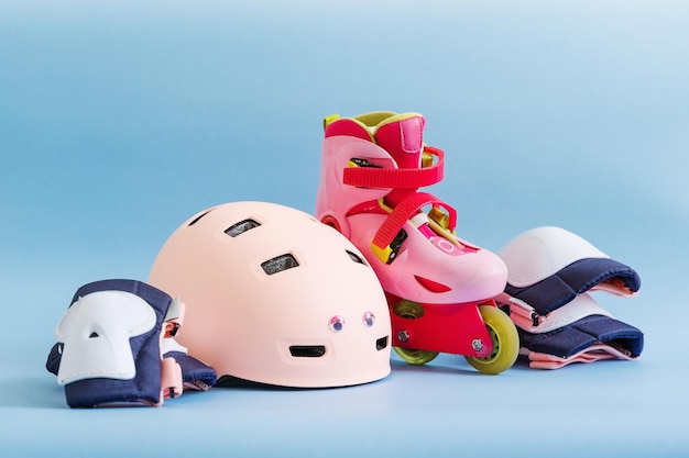 Set of roller skates and protective gear set knee elbow and wrist pads and helmet in pink colors Blue background flat lay