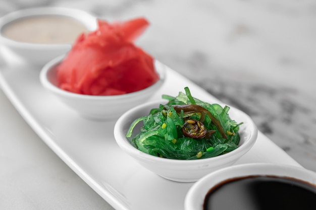 Set of sauces for sushi on a white plate ginger soy sesame seaweed bright textured marble background side view closeup