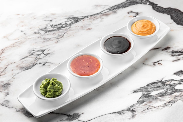 Set of sauces for sushi on a white plate wasabi spicy cheesy soy bright textured marble background side view