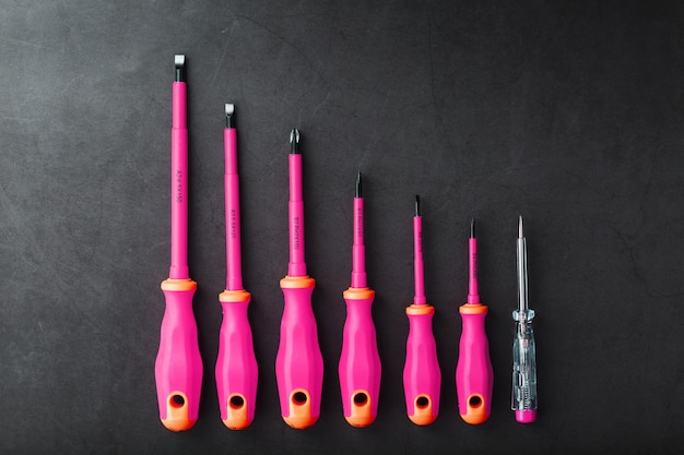 A set of screwdrivers with pink handles in a row on a black background with a free space.