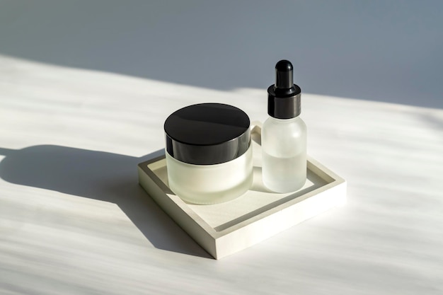 Set of skin care cosmetic products Frosted glass jar and dropper bottle on square concrete tray with harsh shadows Face treatment concept