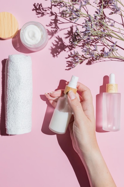 Set of skin care cosmetics in white frosted class package with bamboo lids on pink background Female hand holding a bottle with cream