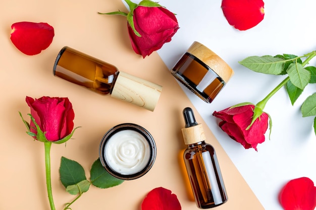 Set of skin care products in dark glass botlles cream serum fluid mask on beige background with red roses Unbranded mockup