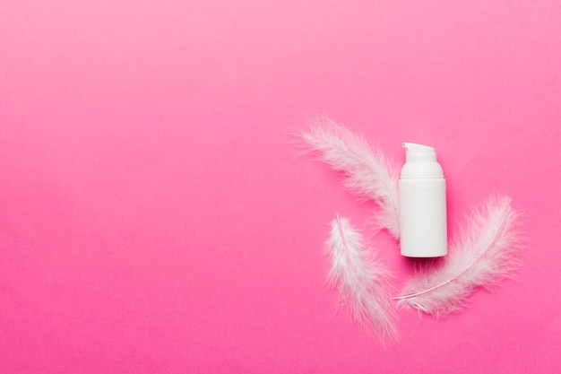 Set of skin care serums on pink pastel background with ostrich feathers Spa cosmetic product cream jar branding mock up top view with copy space