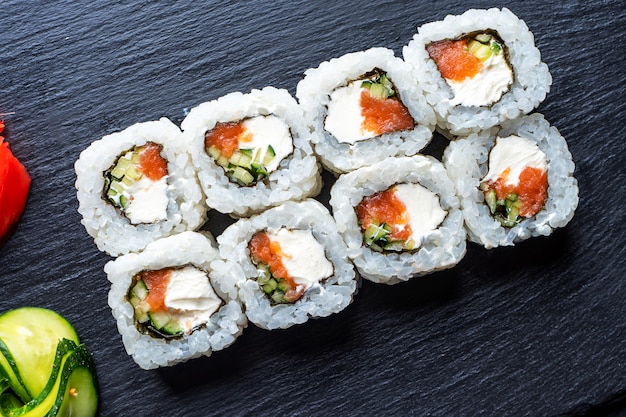 Set of sushi rolls with cream cheese, rice and salmon on a black board decorated with ginger and wassabi on a dark wooden table. Japanese cuisine. Food photo table